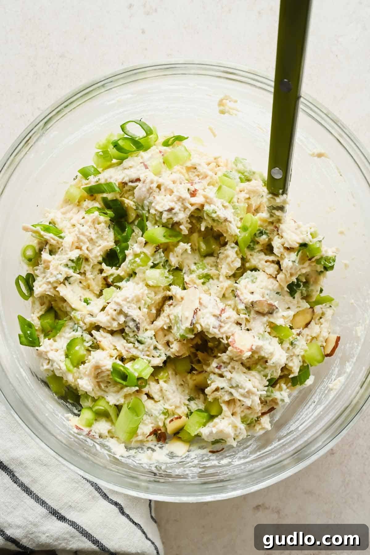 Boursin chicken salad spread fully combined with celery, green onions, and sliced almonds in a glass bowl.