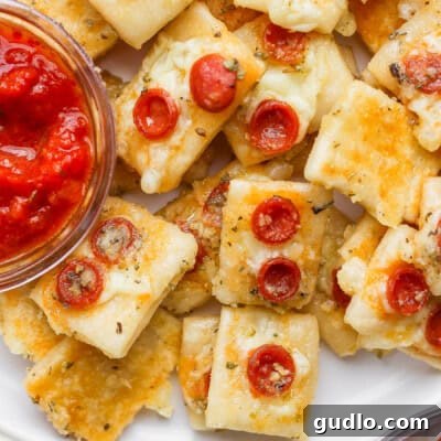 Close-up of mini cheese and pepperoni pizza bites on a plate with a small bowl of marinara dipping sauce.